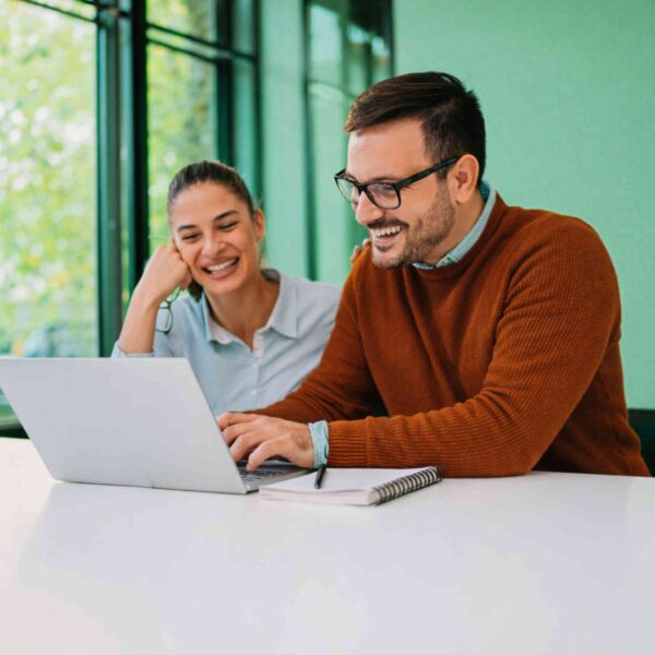 A professional man and woman smiling while working on a laptop for done for you real estate course creation.